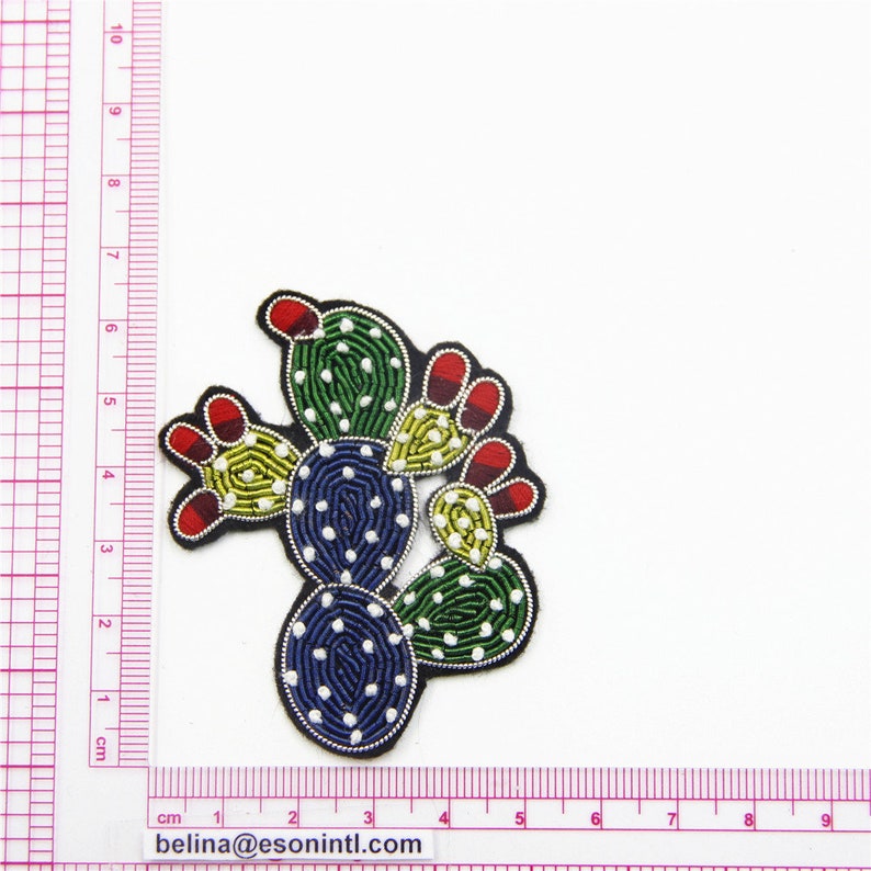 May include: An embroidered cactus patch in green, yellow and blue with red accents. The cactus is surrounded by white dots.