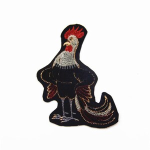 May include: A black embroidered patch of a rooster with a red comb and wattle, standing on a black background.