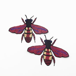May include: Two embroidered bee patches with red wings, yellow and black striped bodies, and blue accents.