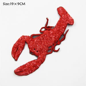 May include: Red sequined lobster applique patch, measuring 19 x 9 cm. The patch is made of red sequins and has a black mesh backing.
