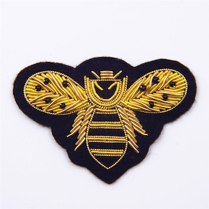 May include: A gold embroidered bee patch on a black felt background. The bee has a detailed design with gold thread and black beads.
