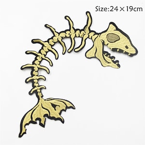 Può includere: Toppa da stirare ricamata in oro di uno scheletro di pesce con un teschio e una pinna caudale dettagliate. La toppa misura 24 x 19 cm.