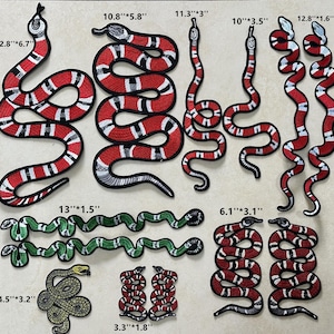 May include: A set of 10 iron-on patches featuring colourful snake designs. The patches are in various sizes, ranging from 3.3 inches to 13 inches. The snakes are in red, black, and white, and green colours.