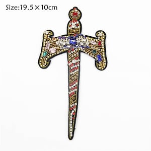 May include: A gold-colored embroidered patch depicting a sword with a cross-shaped handle. The sword is decorated with colorful rhinestones and beads. The patch measures 19.5 inches by 10 inches.