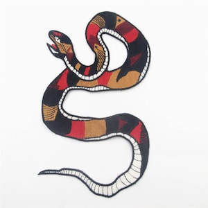 Può includere: Una toppa ricamata da stirare a forma di serpente rosso, nero e marrone con contorno bianco. Il serpente è arrotolato in un cerchio con la testa rivolta a sinistra.