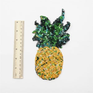 Può includere: Un toppa a forma di ananas di paillettes gialle e verdi. L'ananas è alta circa 7,5 cm e larga 5 cm.