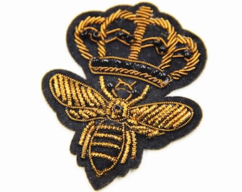 May include: A gold embroidered bee with a crown on its head. The bee and crown are sewn onto a black felt patch. Size: 4.5 x 5.5 cm.
