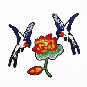 May include: Three embroidered iron-on patches featuring a red and yellow lotus flower and two blue and white birds. The birds are flying towards the flower.