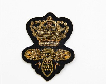 May include: A black felt patch with a gold embroidered crown and bee design. The crown is adorned with rhinestones and the bee has gold wings and a body.