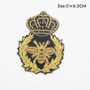 Peut inclure: Un patch brodé or avec une couronne, une abeille et une couronne de feuilles sur fond noir. Taille : 5 x 6,5 cm.