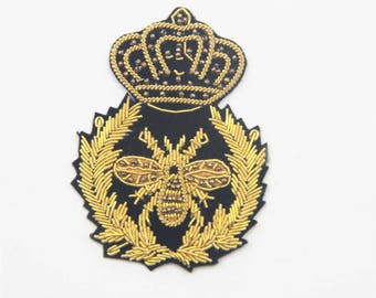 May include: A gold embroidered patch featuring a crown, a bee, and a wreath of leaves on a black background. Size: 5 x 6.5 cm.