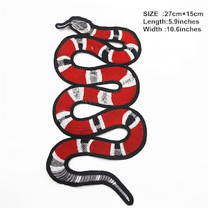 May include: Embroidered snake patch in red, black, and white. The snake design is approximately 10.6 inches wide and 5.9 inches long. The patch features a detailed design with a textured appearance, suitable for clothing or accessories.