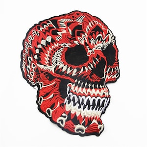 Könnte beinhalten: Roter und weißer gestickter Totenkopf-Patch auf schwarzem Hintergrund. Der Totenkopf ist mit komplizierten Mustern und einem wilden Ausdruck verziert.