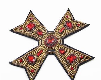 May include: A gold and red cross-shaped patch with a beaded design and red rhinestone accents.