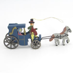May include: A blue wooden toy carriage with a horse. The carriage has a driver and a passenger. The horse is gray and brown, and the carriage has black wheels. A gold string is attached to the top.