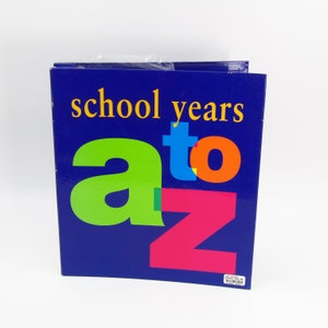 May include: A blue binder with the words "school years" in yellow and "a to z" in green, blue, orange, and pink. The binder is sealed in plastic and sits on a white surface. The binder is for school.