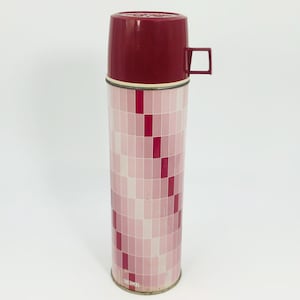 May include: A vintage Thermos brand vacuum flask. The flask has a burgundy lid and handle, with a pink and red geometric pattern on the body. The base is metallic.