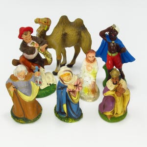 May include: A collection of painted figurines depicting a nativity scene. The figures include a camel, a musician, the Virgin Mary, the three wise men, and other biblical characters. The figurines are brightly colored and made of a hard material.