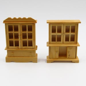 May include: Two wooden cabinets with glass doors and shelves. The cabinet on the left has a drawer and a slightly curved base. The cabinet on the right has a solid bottom with two doors.