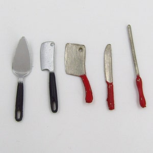 May include: A collection of miniature kitchen utensils, including a pie server, cleavers, and knives. The handles are black or red, and the blades are silver. The set is arranged on a white surface.