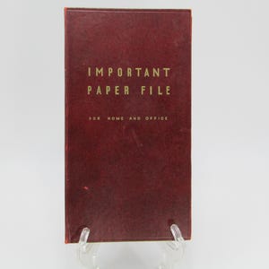 May include: A red, leather-bound book with the title "IMPORTANT PAPER FILE FOR HOME AND OFFICE" in gold lettering.