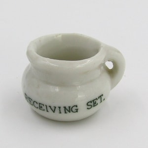 May include: White ceramic chamber pot with a handle and the words "RECEIVING SET" printed in green on the side.