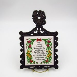 May include: A black cast iron trivet with a rooster design on top. The trivet holds a white ceramic tile with a floral border and a poem that reads: "My house is small - No mansion for a millionaire - But there is room for love And there is room for friends That's all I care."