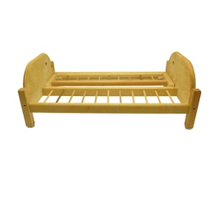 May include: A small, unfinished wooden doll bed. The bed frame is light brown with a slatted base and headboard. The bed is approximately 12 inches long and 8 inches wide.