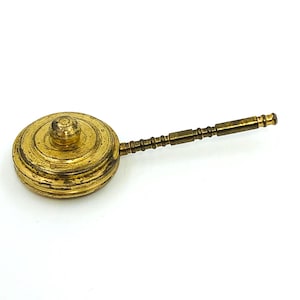 May include: A vintage brass instrument with a circular, lidded body and a long, slender handle. The brass has a warm, aged patina, suggesting its antique nature. The handle is segmented, adding to its unique design. The object is likely a measuring tool or a small cooking utensil.
