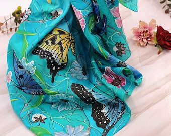 May include: A turquoise silk scarf with a floral and butterfly design. The scarf features a variety of butterflies in different colors and patterns, including yellow, black, and blue. The flowers are pink, white, and blue.