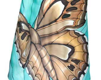 May include: A silk scarf with a large butterfly design. The butterfly wings are brown, tan, and white, set against a turquoise background. The scarf is draped over a form, showcasing the artwork.