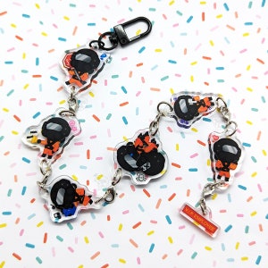 May include: A clear acrylic charm bracelet with six charms featuring cartoon characters wearing black helmets and orange jumpsuits. The charms are connected by silver jump rings. The bracelet has a black lobster clasp and a small charm that says "VIP Employee".