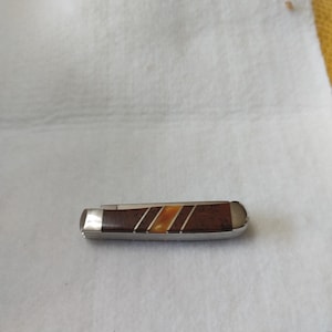 May include: A small, closed pocket knife with a brown handle featuring three diagonal stripes in shades of tan and orange. The knife has a silver-colored bolster and end cap. The blade is not visible in this image.