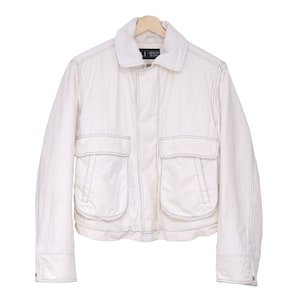 May include: A white jacket with a collar, two front pockets, and visible stitching. The jacket is hanging on a wooden hanger. The brand name "Armani Jeans" is visible on the collar.