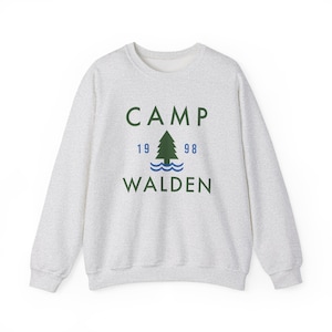 Può includere: Una felpa grigia con un pino verde e il testo "CAMP 19 98 WALDEN" stampato sul davanti.