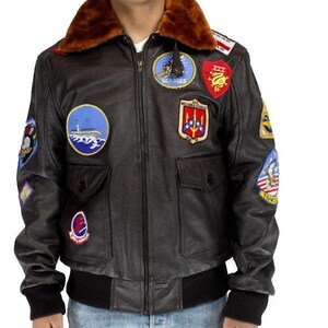 May include: A dark brown leather jacket with a brown fur collar and various embroidered patches. The jacket features a zip closure, two front pockets, and black ribbed cuffs and waistband. Patches display military and aviation-related designs.