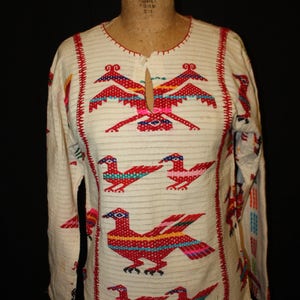 May include: A white cotton blouse with a crew neck and long sleeves. The blouse is embroidered with colorful birds and geometric patterns.