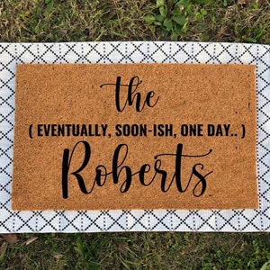 May include: A brown coir doormat with white fringe. The text on the doormat reads "the (eventually, soon-ish, one day...) Roberts"
