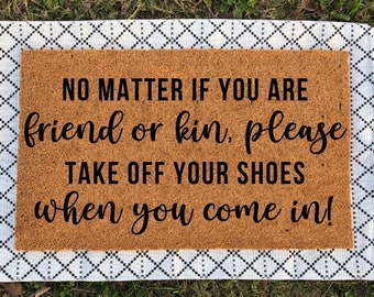 May include: A brown coir doormat with white fringe. The doormat has the text "NO MATTER IF YOU ARE friend or kin, please TAKE OFF YOUR SHOES when you come in!" printed in black.