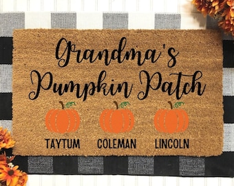Puede incluir: Una alfombra de coco marrón con el texto "Grandma's Pumpkin Patch" en letra cursiva negra. Tres calabazas naranjas con tallos verdes están dispuestas debajo del texto, cada una con un nombre debajo: Taytum, Coleman y Lincoln.