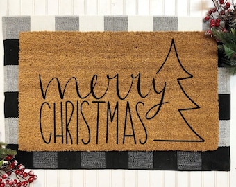 May include: A brown coir doormat with black text that reads "merry christmas" and a stylized black Christmas tree design.