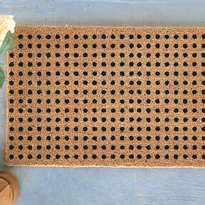 May include: Rectangular doormat made from natural coir fibre, featuring a repeating pattern of black dots. The mat is a light brown colour and is designed for outdoor use. The doormat is approximately 61 cm long and 41 cm wide.