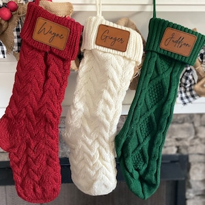 May include: Three knitted Christmas stockings with personalised leather name tags. The stockings are red, white, and green. The names on the tags are Wayne, Ginger, and Judson.
