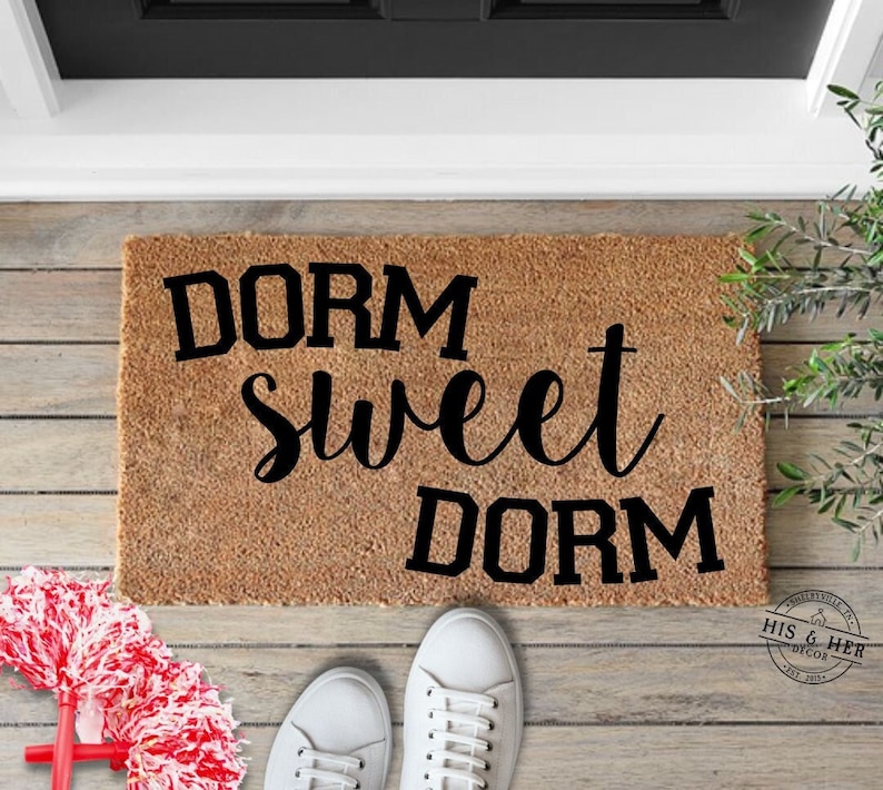 May include: A brown coir doormat with the text "Dorm Sweet Dorm" in black lettering.