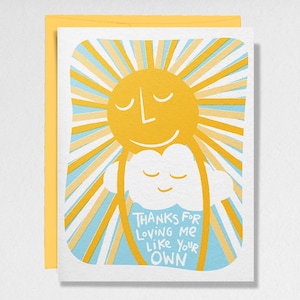 Peut inclure: Carte de vœux avec une illustration d'un soleil jaune et d'un nuage blanc. Le soleil a un visage souriant avec les yeux fermés et des rayures jaunes et bleues rayonnantes. Le nuage a un visage souriant et le texte "THANKS FOR LOVING ME LIKE YOUR OWN". La carte est dans une enveloppe jaune.