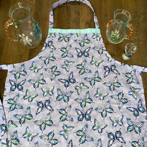 May include: A purple apron with a light blue trim and a butterfly pattern. The butterflies are blue, green, and white.