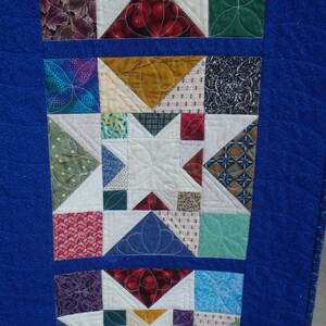 Puede incluir: Una tela acolchada azul con un patr&oacute;n de cuadrados y estrellas de colores. La tela est&aacute; compuesta por diferentes patrones y colores, incluyendo rojo, verde, azul, blanco y marr&oacute;n.