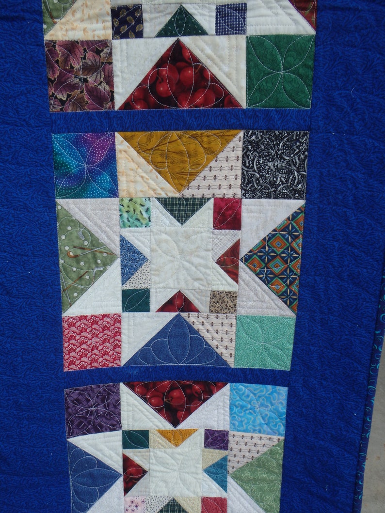 Puede incluir: Una tela acolchada azul con un patr&oacute;n de cuadrados y estrellas de colores. La tela est&aacute; compuesta por diferentes patrones y colores, incluyendo rojo, verde, azul, blanco y marr&oacute;n.