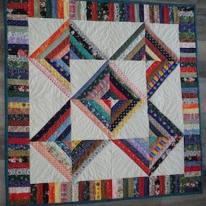 May include: A colorful quilt with a patchwork design featuring a variety of fabrics in different colors and patterns. The quilt is made up of squares and triangles, and the edges are trimmed with a teal border.