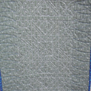 Puede incluir: Primer plano de una tela acolchada verde con un patr&oacute;n geom&eacute;trico blanco. La tela est&aacute; cosida con hilo blanco, creando un dise&ntilde;o detallado.